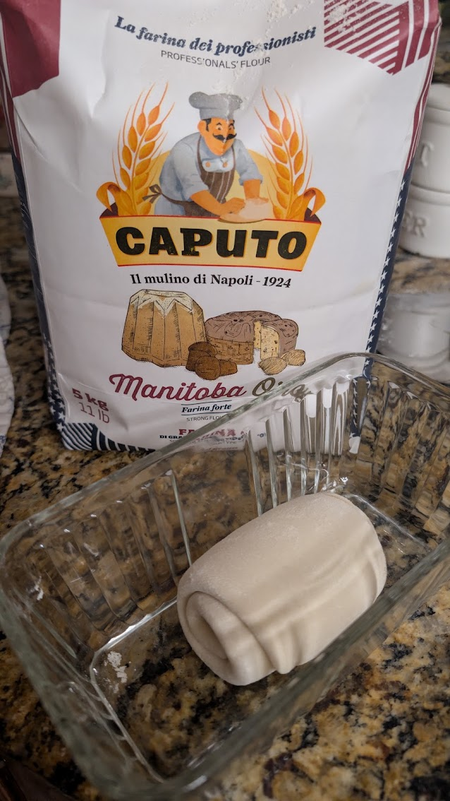 Fresh lievito madre dough in a glass dish with a bag of Caputo Manitoba Oro flour behind it
